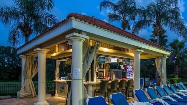 A covered outdoor seating area with lounge chairs and a bar. - Kissimmee townhouse w/ shared pool & BBQ (Kissimmee)
