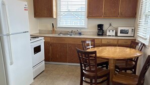 Une cuisine compacte avec des meubles en bois, un réfrigérateur blanc, une cuisinière, un évier et une table à manger avec des chaises.