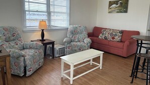 Un salon avec deux fauteuils à motifs, une table basse blanche, un canapé rouge et un tableau accroché au mur.