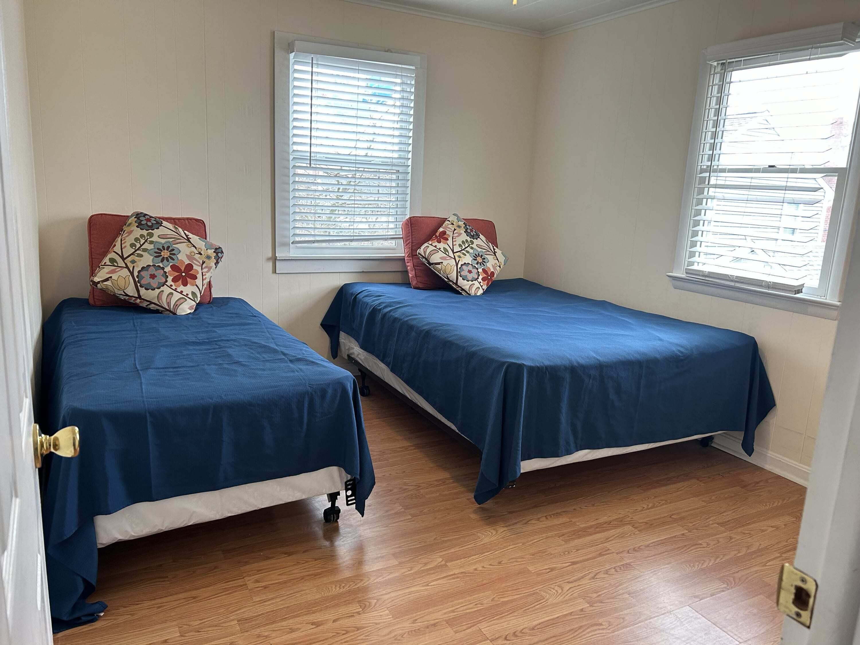 A room with two single beds, wooden flooring, and windows with blinds.