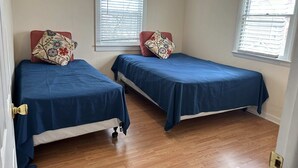 Une chambre avec deux lits simples, un plancher en bois et des fenêtres équipées de stores.