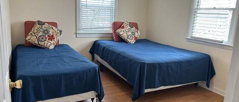 A room with two single beds, wooden flooring, and windows with blinds.