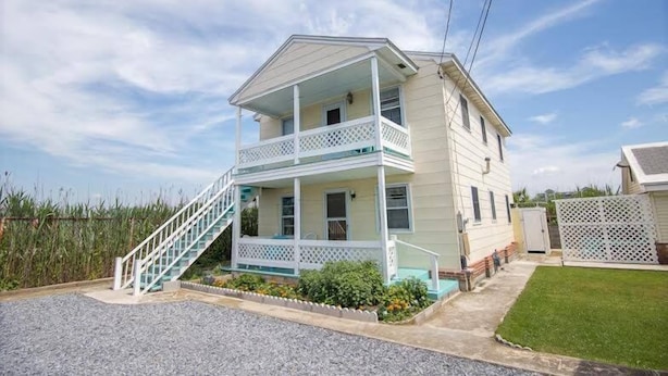 Une maison à deux étages avec un porche à l’avant, un escalier et un petit jardin devant.