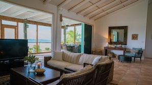 A living room with a television, wicker furniture, a sofa, and a view of the beach.
