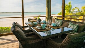 Un comedor con mobiliario de mimbre, una mesa de vidrio y vista a la playa.