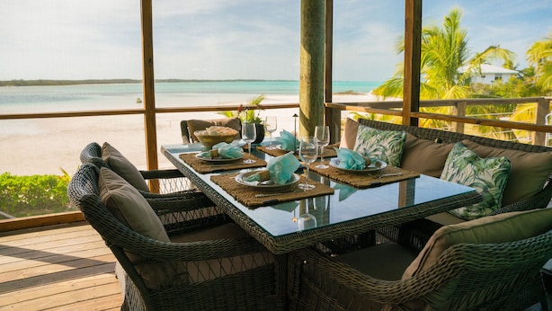 A dining area with wicker furniture, a glass table, and a view of the beach.