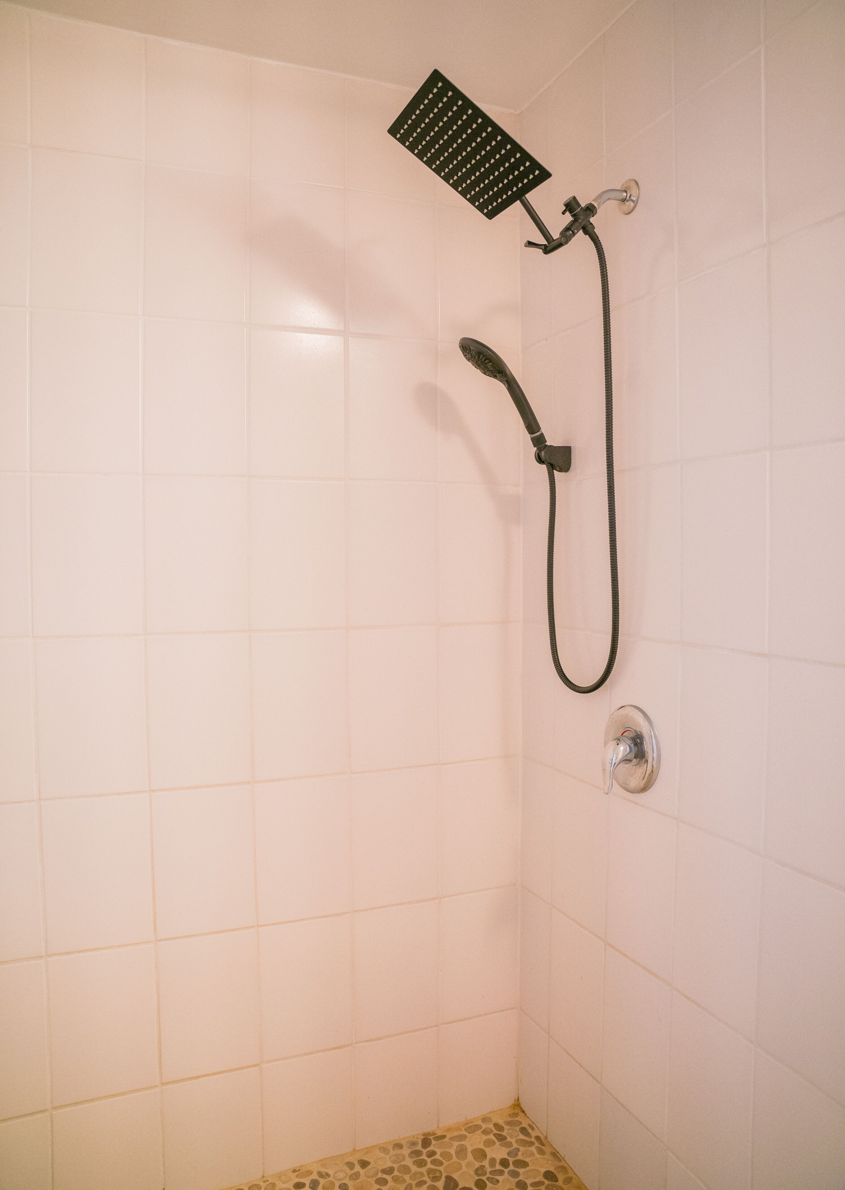 A shower with a handheld showerhead and a fixed wall-mounted showerhead in a tiled room.