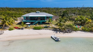 A beachfront property with a large house, a boat docked on the sand, and several colorful chairs.