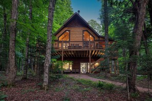Una cabana de fusta de dos pisos amb un balcó, envoltada per un bosc.