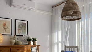 A dining area with a wooden table and chairs, a hanging wicker light fixture, and a white air conditioning unit on the wall. - Les Doyes 116 (Peníscola)