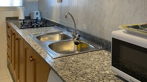 A kitchen with granite countertops, stainless steel appliances, wooden cabinets, and a window with blinds. - Les Doyes 116 (Peníscola)