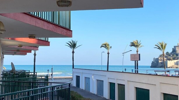 A coastal view from a balcony overlooking the sea, with a building featuring multiple doors and a satellite dish. - Les Doyes 116 (Peníscola)
