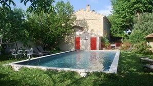 Une piscine rectangulaire bordée de pierres, entourée de pelouse et d’arbres.