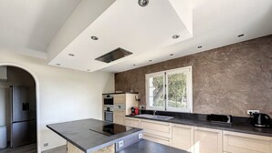 A modern kitchen with a large island, built-in appliances, and a view of the outdoors through a window. - Maison Familiale Avec Piscine et Magnifique Jardin, Sud de la France (Piolenc)