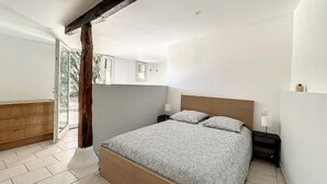 A bedroom with a large bed, wooden headboard, and a nightstand with a lamp. There is a wooden dresser and a window with a view of trees. - Maison Familiale Avec Piscine et Magnifique Jardin, Sud de la France (Piolenc)