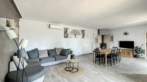 A modern living room with a grey sectional sofa, a round coffee table, a dining table with chairs, a flat-screen TV, and a fireplace. - Maison Familiale Avec Piscine et Magnifique Jardin, Sud de la France (Piolenc)