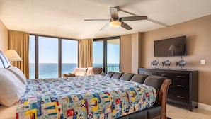 Ein Hotelzimmer mit einem großen Bett, einem Deckenventilator, einem Fernseher, einem Schminktisch und Blick auf das Meer.