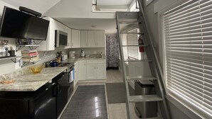 Une cuisine compacte avec des meubles blancs, un four à micro-ondes, un évier et un petit îlot central doté d’un plan de travail en marbre.