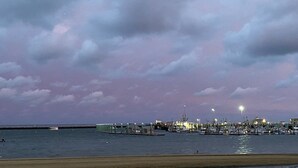 Un port de plaisance au crépuscule, avec des bateaux amarrés, une digue et une côte lointaine.