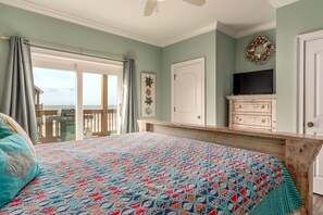 Un dormitorio con cama, cómoda, televisor y vista al océano.