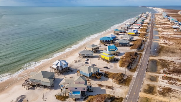 Luchtbeeld van een kustgebied met strandhuisjes, een weg en een strand.
