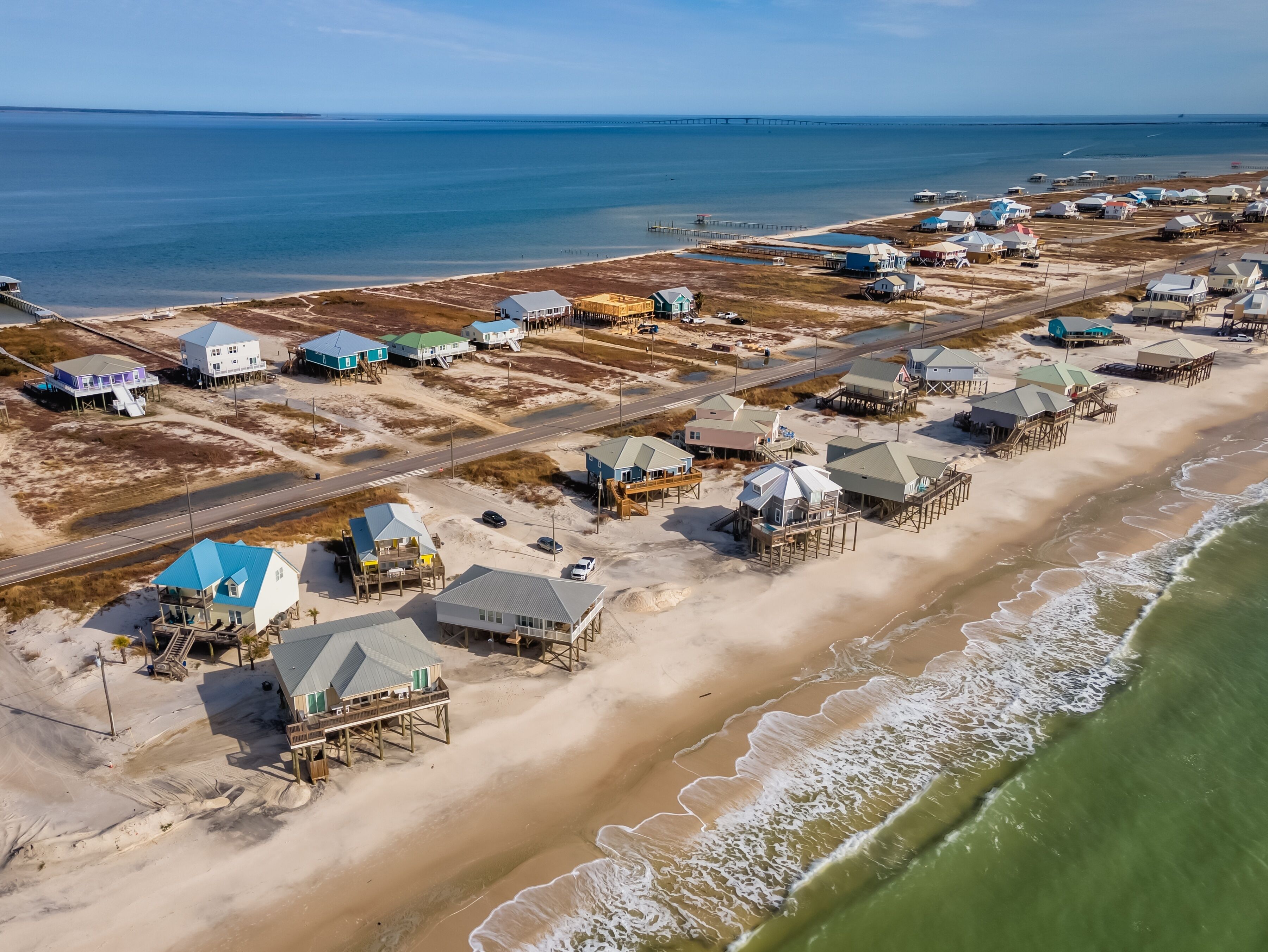An aerial view of a coastal area with beach houses and a pier.