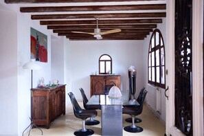 A dining area with a wooden ceiling, a ceiling fan, a wooden cabinet, a glass table, and four black chairs. - Villa au Bord de la mer à 5mn des Calanques et du Centre Ville, Dans un Parc (La Ciotat)