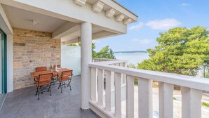 A balcony with a stone wall, wooden furniture, and a view of the sea. - Cozy apartment in Mrljane (Mrljane)