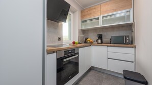 A modern kitchen with white cabinets, a black oven, a microwave, and a coffee maker. - Cozy apartment in Mrljane (Mrljane)