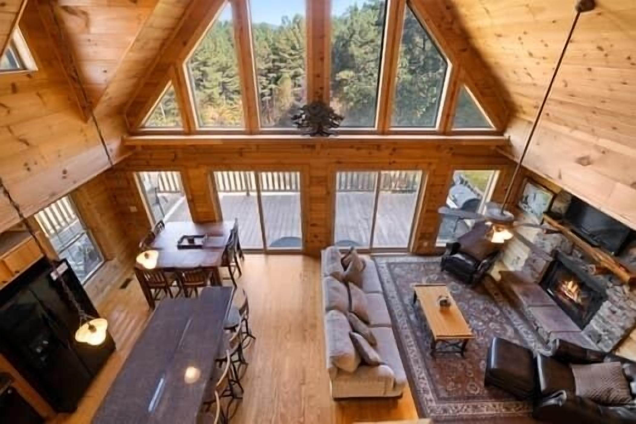 Een houten cabin interieur met een eethoek, bank, open haard en grote ramen met uitzicht op het bos.