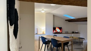 A modern dining area with a wooden table and chairs, a TV displaying a fire, and a kitchen in the background. - LYON PRESQU ILE musée des tissus - Air-conditioned APARTMENT ideal for visiting LYON (Lyon)