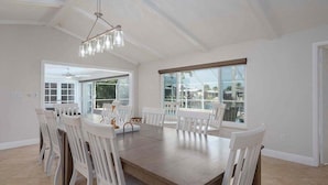 A dining area with a large table, white chairs, and a hanging light fixture.