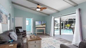 En rummelig stue med ventilator, udsigt til pool og dør til balkon.