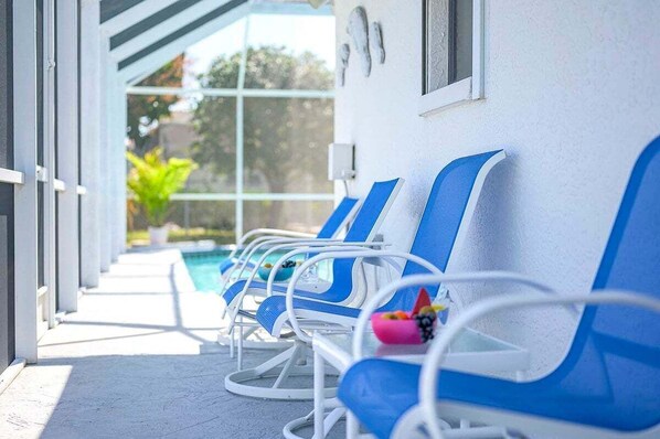 Una hilera de sillones reclinables azul y blanco junto a una piscina, con vistas despejadas a la piscina y vegetación al fondo.