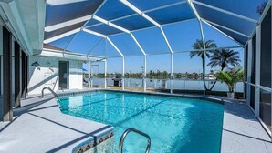 En swimmingpool med et glasindhegning, et område ved poolen og udsigt til vandet.