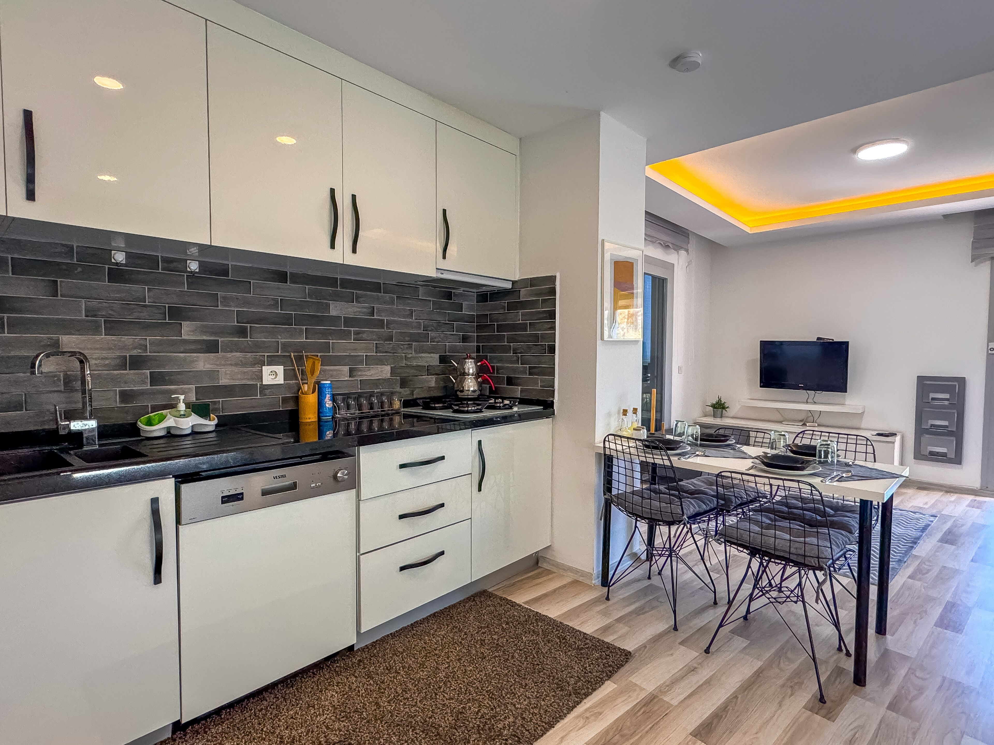 A modern kitchen with white cabinets, a black countertop, and a dining area with a table and chairs.