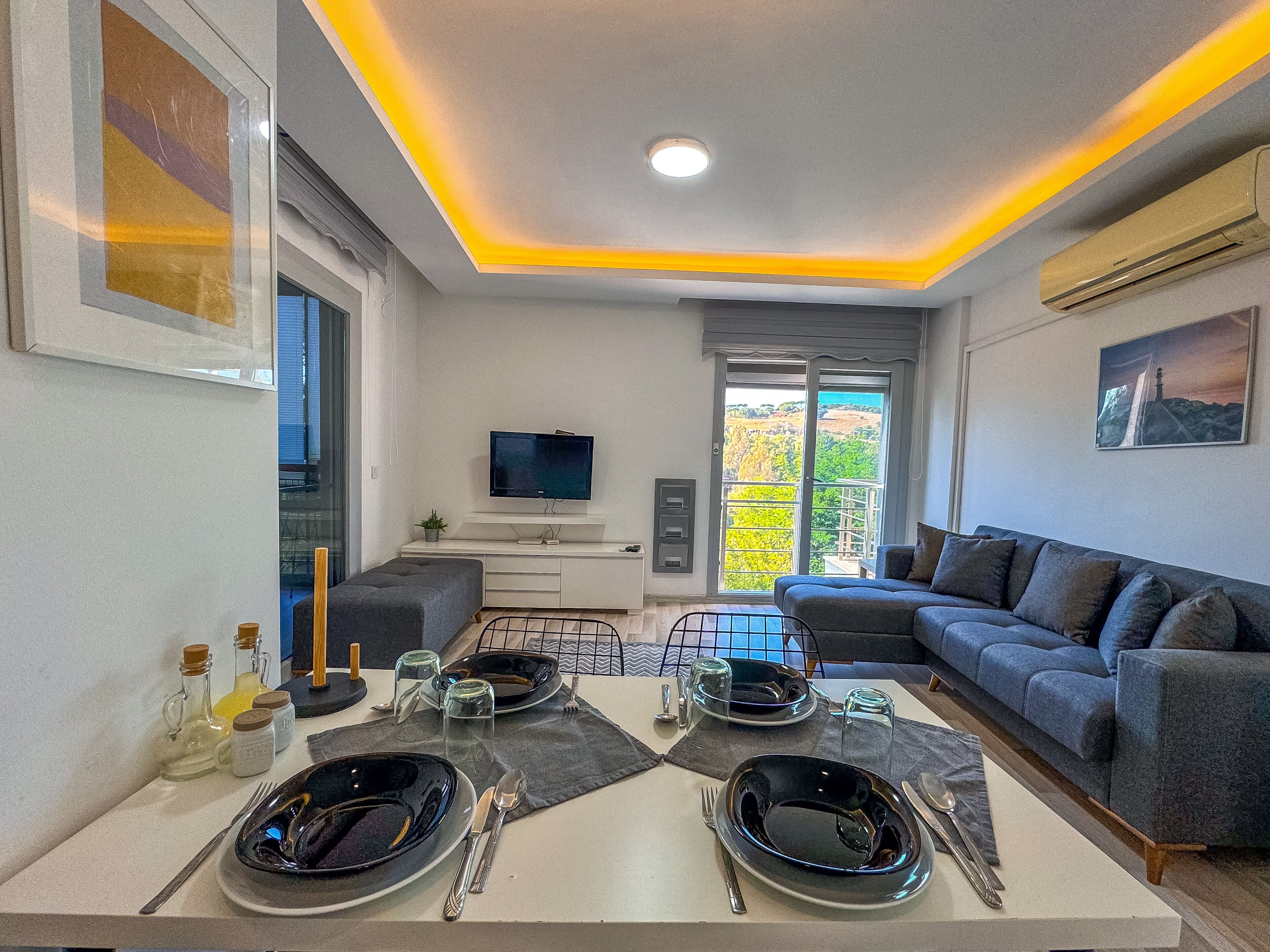 Un salon moderne avec un canapé, un téléviseur à écran plat et une table à manger dressée pour deux personnes.