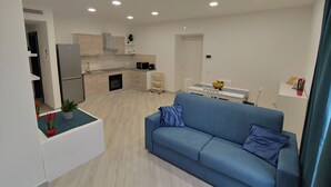 Una sala de estar moderna con un sofá azul, una cocina con armarios blancos y un comedor con una mesa blanca.