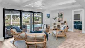 A spacious living area with wicker furniture, a view of a pool, and a modern ceiling design. - Luxury Golf-View Oasis with Heated Pool & Quiet Marco Island Location (Marco Island)