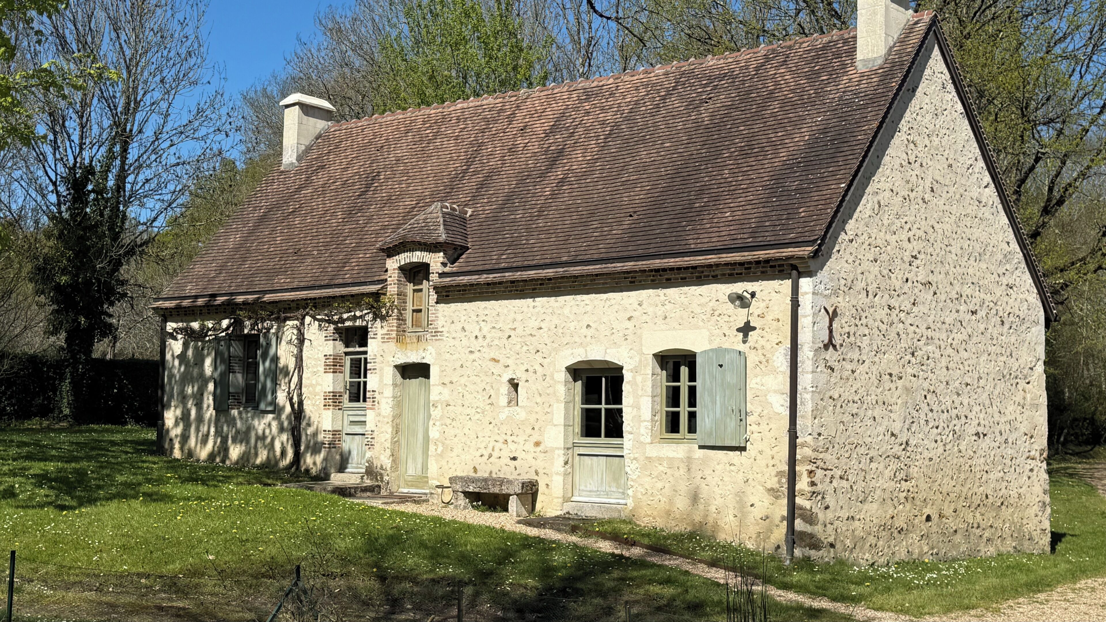 Une maison en pierre avec un toit en tuiles, une cheminée et un petit porche.
