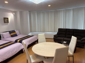 Ein Hotelzimmer mit zwei Betten, einem Sofa, einem runden Tisch und einem Fenster mit Jalousien.