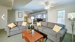 A living room with two grey sofas, a wooden coffee table, and a ceiling fan. - Beautiful resort at OBX, NC. Beach access, 3 bedrooms, 2 bath,  7/7-7/14. (Kitty Hawk)