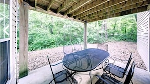 An outdoor patio with a glass-top table and metal chairs, surrounded by a wooden pergola and a view of a wooded area. - Beautiful resort at OBX, NC. Beach access, 3 bedrooms, 2 bath,  7/7-7/14. (Kitty Hawk)