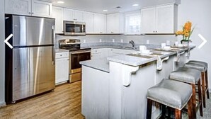 A modern kitchen with white cabinets, stainless steel appliances, and a central island with bar stools. - Beautiful resort at OBX, NC. Beach access, 3 bedrooms, 2 bath,  7/7-7/14. (Kitty Hawk)