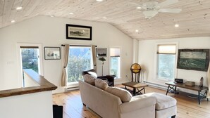 A spacious living room with a large sofa, wooden flooring, and a ceiling fan. - 2 bedroom w/ expansive water views (Phippsburg)