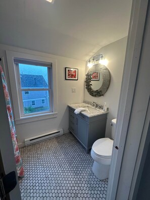 A bathroom with a window, a sink, a toilet, and a mirror with lights. - 2 bedroom w/ expansive water views (Phippsburg)