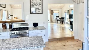 A modern kitchen with granite countertops, a stainless steel range, and a wooden dining area with a view. - 2 bedroom w/ expansive water views (Phippsburg)