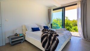 Une chambre moderne avec un grand lit, une table de chevet et une vue sur la verdure par la fenêtre.