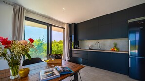 Une cuisine moderne avec des meubles de couleur sombre, un réfrigérateur en acier inoxydable et un coin repas comprenant une table et des chaises en bois.