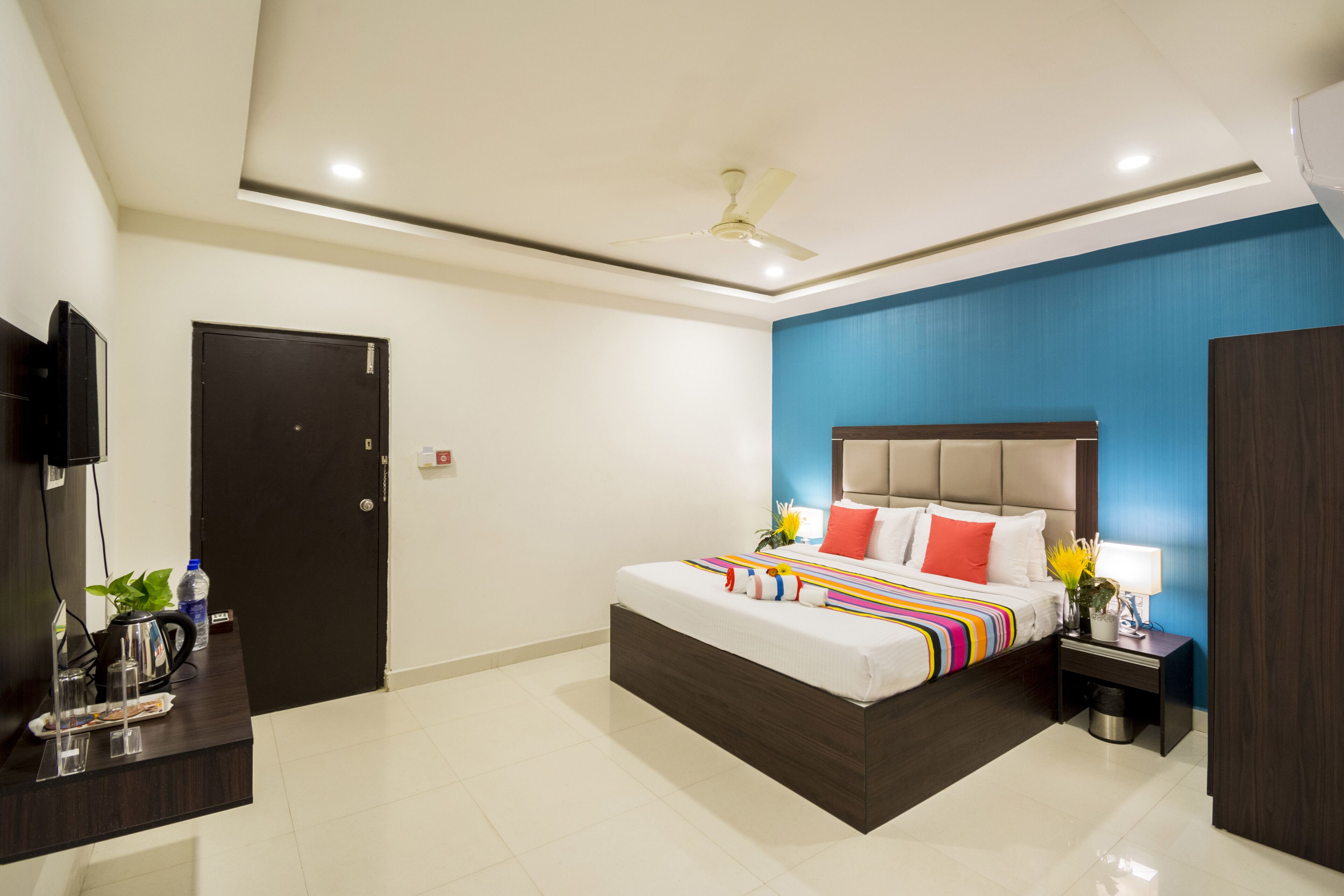 Habitación de hotel moderna con una cama grande, ventilador de techo, televisor y escritorio con una planta.